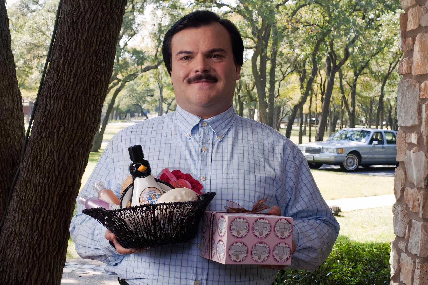 Bernie Tiede smiles while holding gifts outside a home in Richard Linklater’s Bernie.