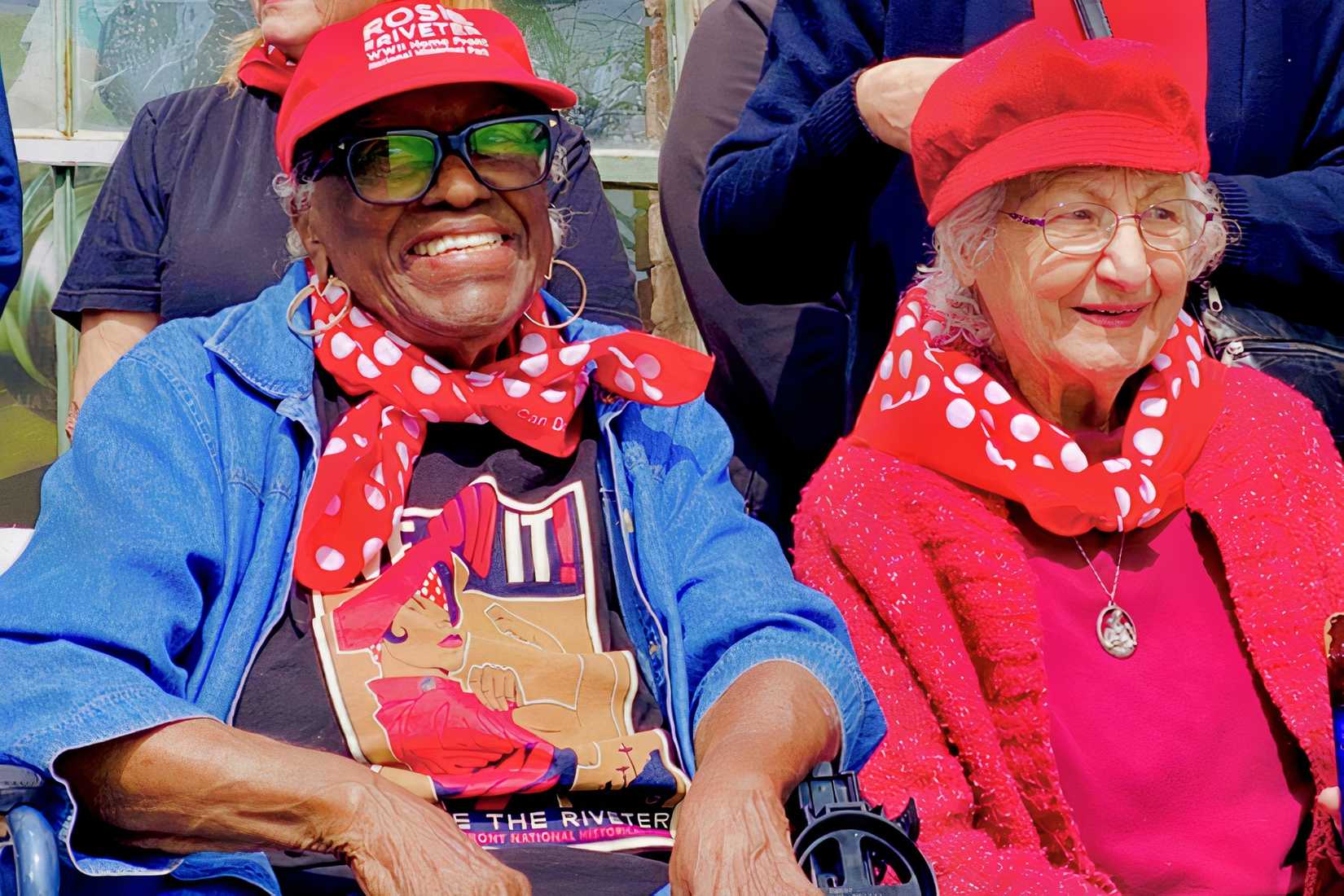 Elizabeth Tate sits beside another Rosie the Riveter while wearing red Rosie-themed clothing.