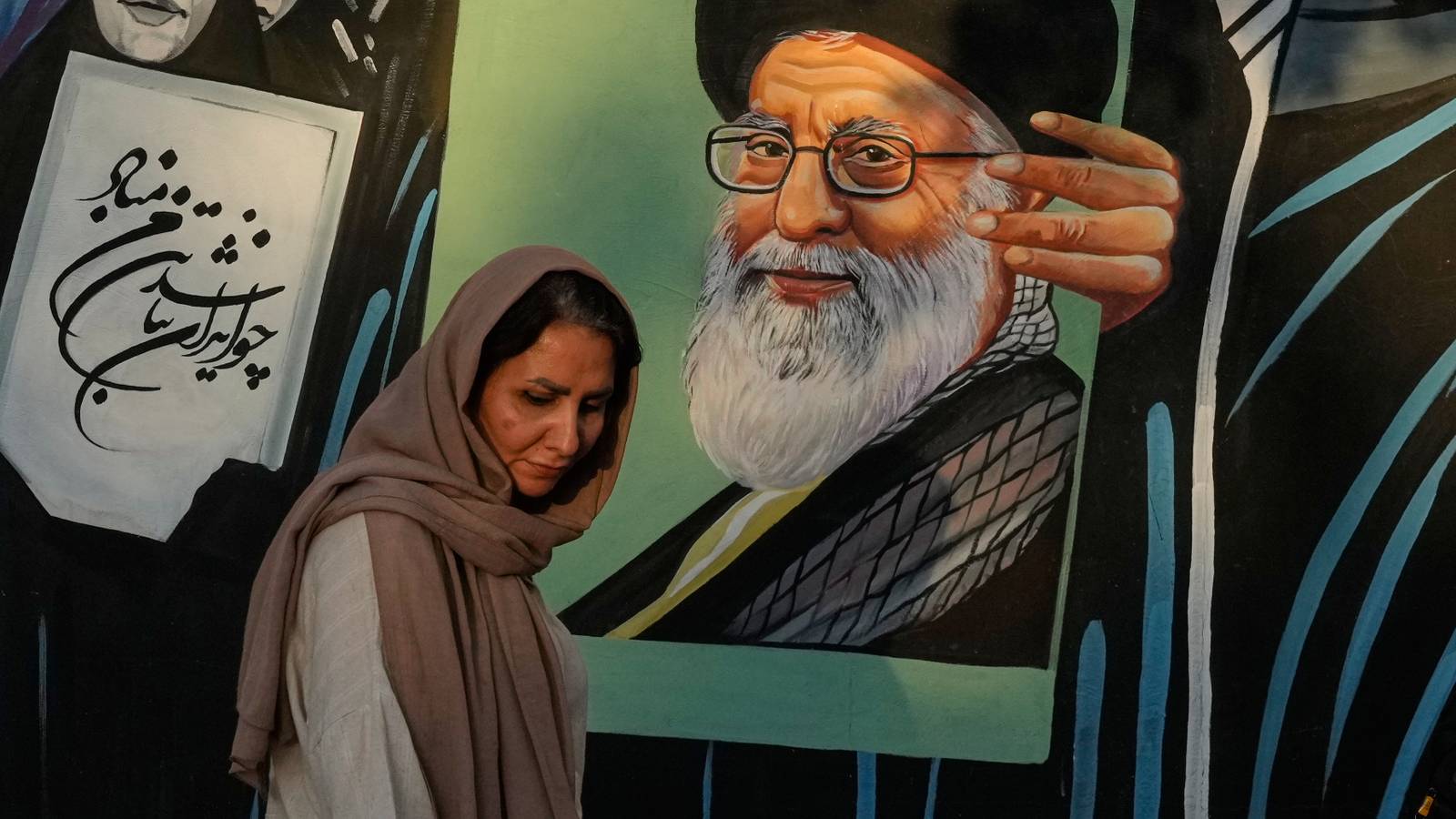 A woman walks past a mural depicting a portrait of the late Iranian Supreme Leader Ayatollah Ali Khamenei.