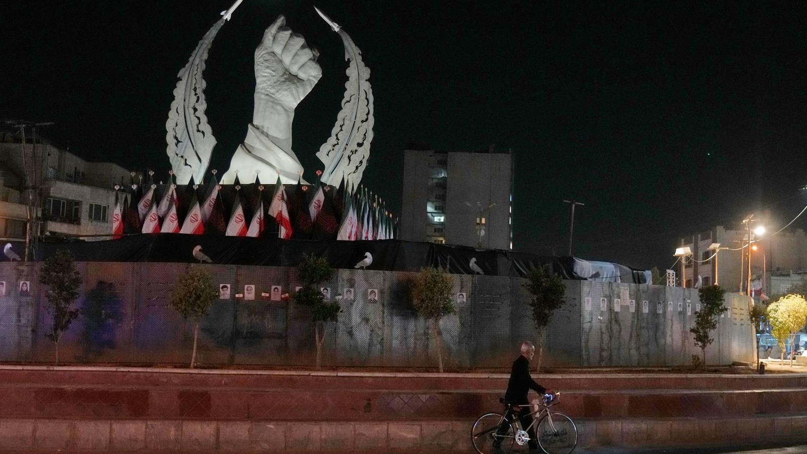 A man carries his bicycle in front of a monument in Iran. 