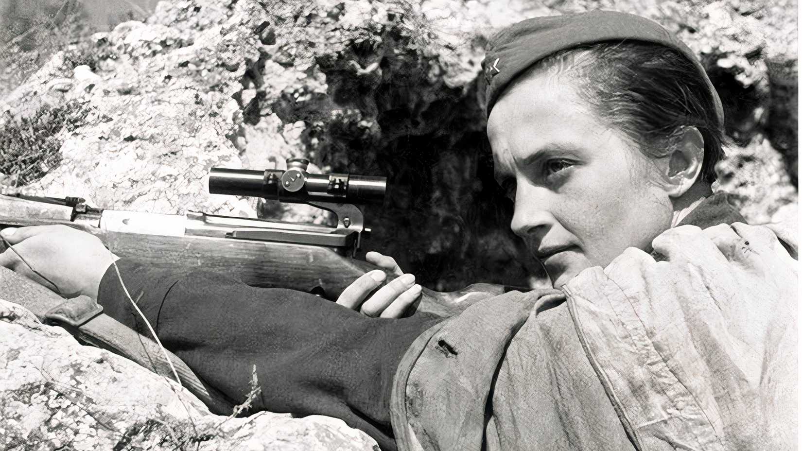 Soviet sniper Lyudmila Pavlichenko rests beside a scoped rifle in a rocky trench during World War II.