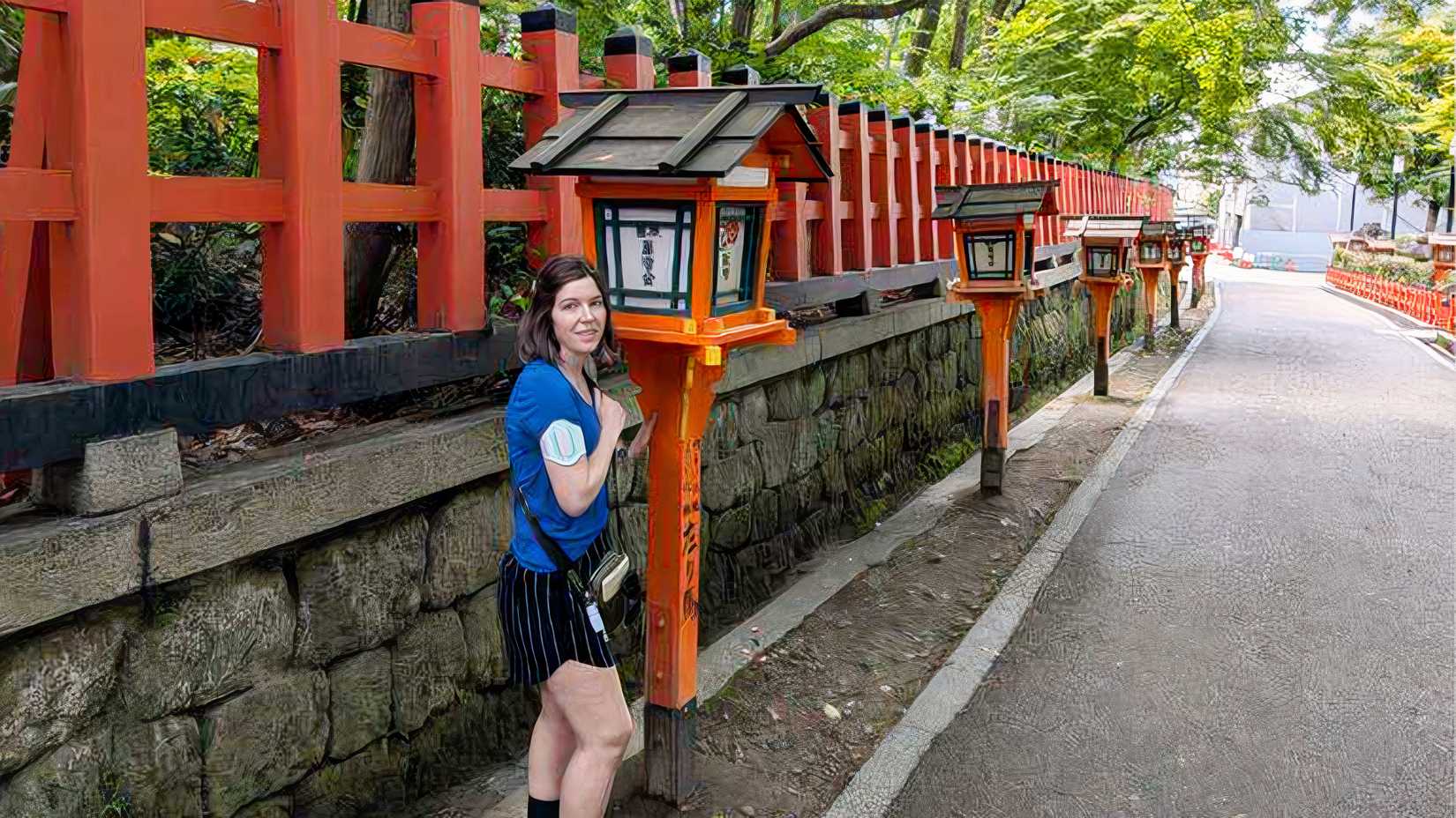 TJ stands beside red shrine lanterns in Japan with a Nerivio device attached to her upper arm.