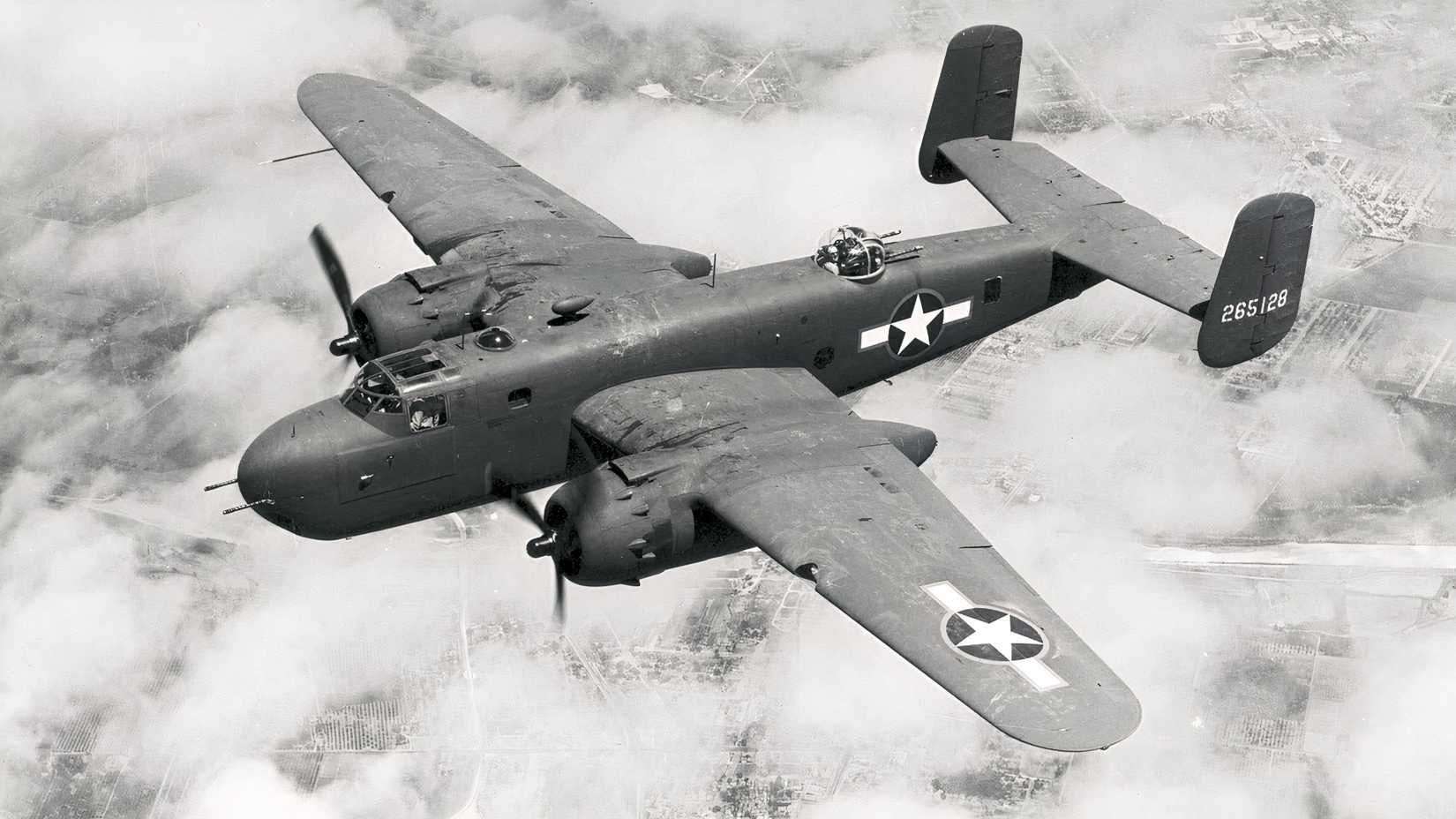 A World War II-era bomber flies above clouds with U.S. military markings visible on its wings and fuselage.