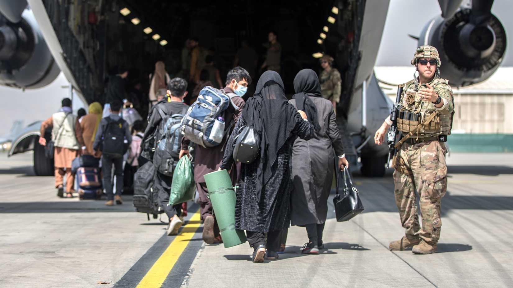 Afghan evacuees carrying bags walk up the ramp of a U.S. Air Force C-17 Globemaster III at Kabul airport.