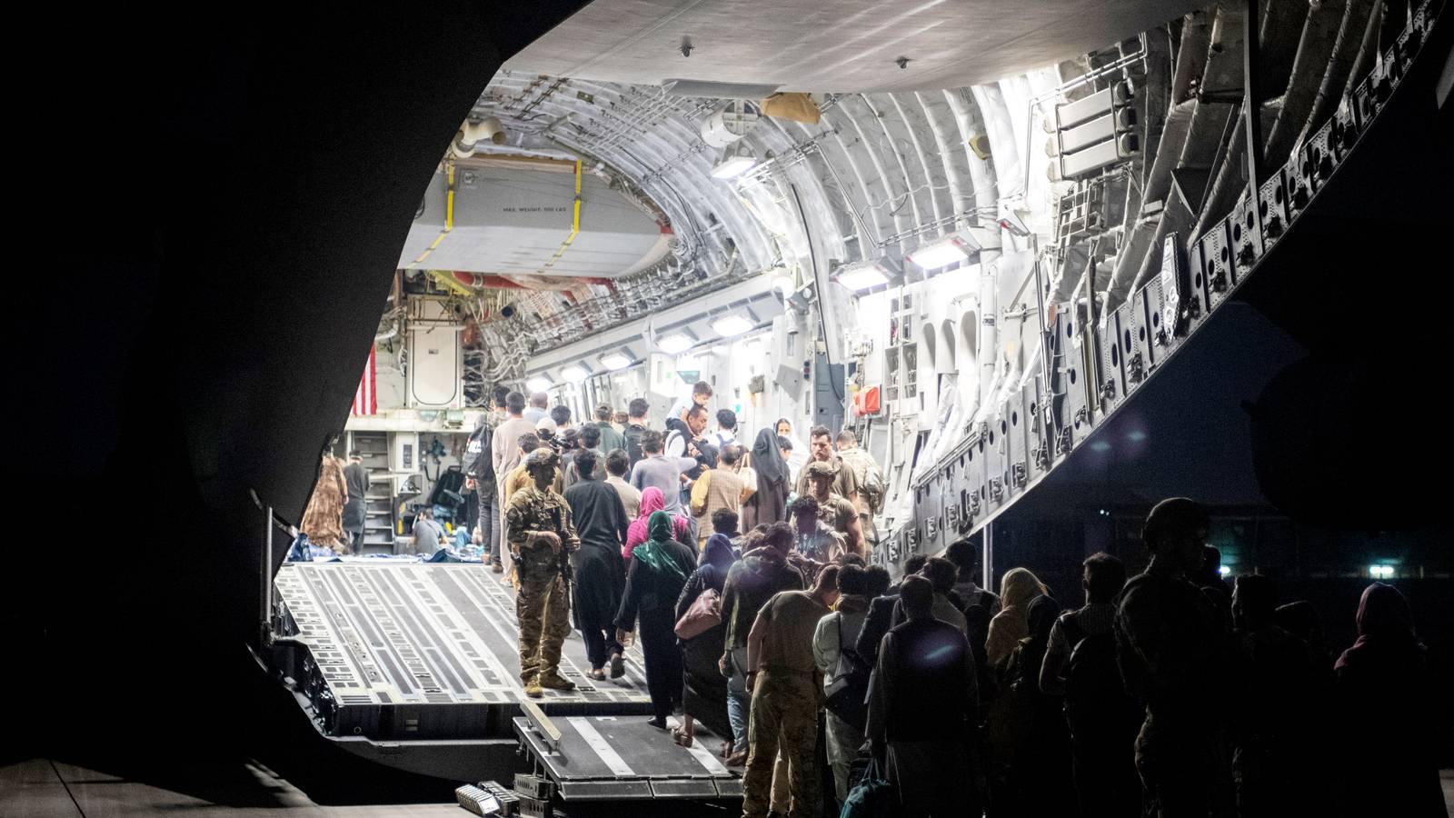 Afghan evacuees line up at night to board a brightly lit U.S. Air Force C-17 Globemaster III at Kabul airport.