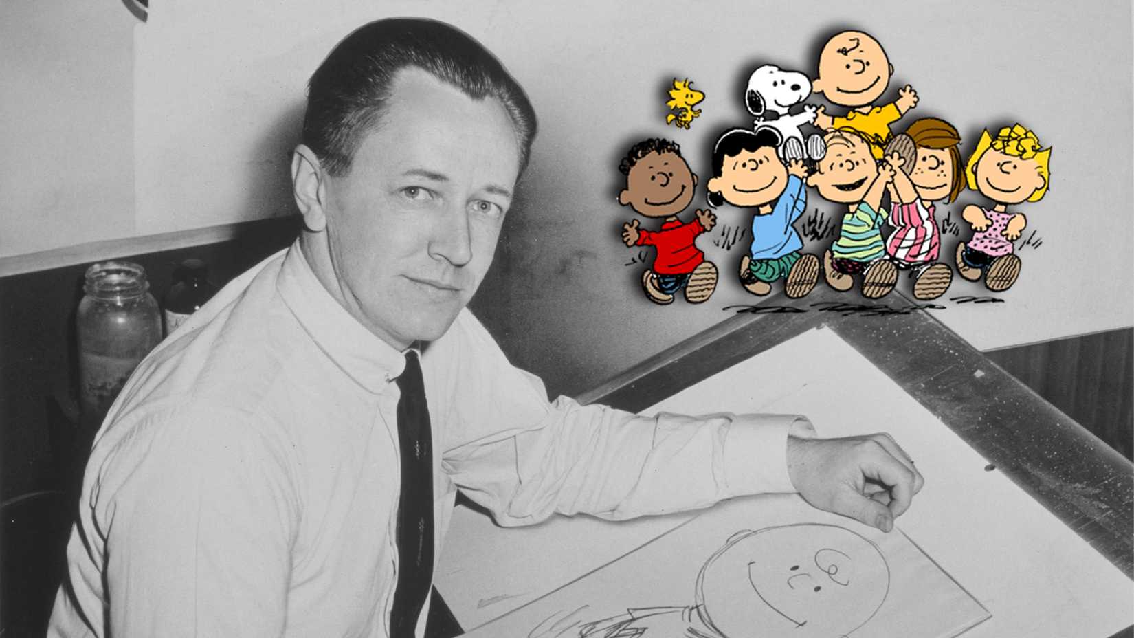 Peanuts creator Charles M. Schulz sits at his drawing board with Charlie Brown, Snoopy and other Peanuts characters.