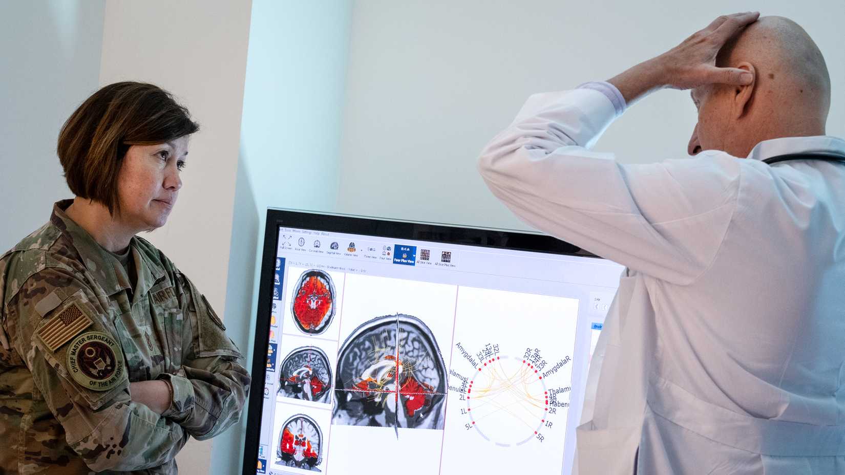 Air Force senior enlisted leader speaks with a medical specialist beside brain scans during a traumatic brain injury briefing at Eglin Air Force Base.