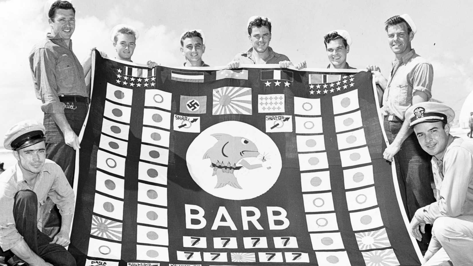 Eight USS Barb demolition squad members pose with the submarine’s decorated battle flag in 1945.