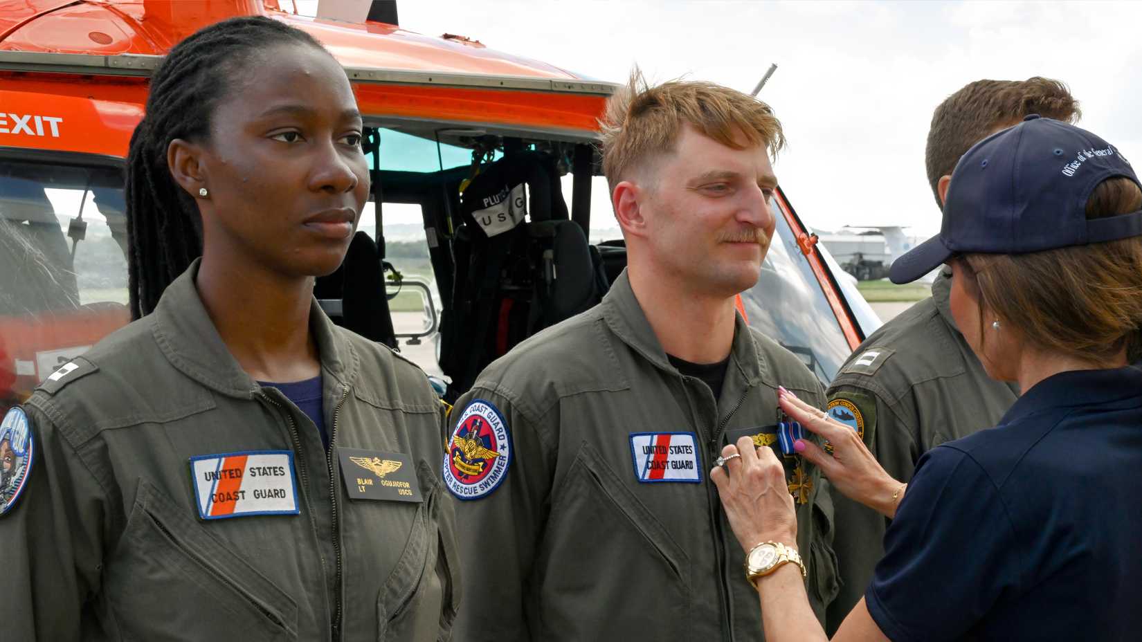A Coast Guard rescue swimmer receives the Distinguished Flying Cross beside an orange rescue helicopter in Kerrville, Texas.
