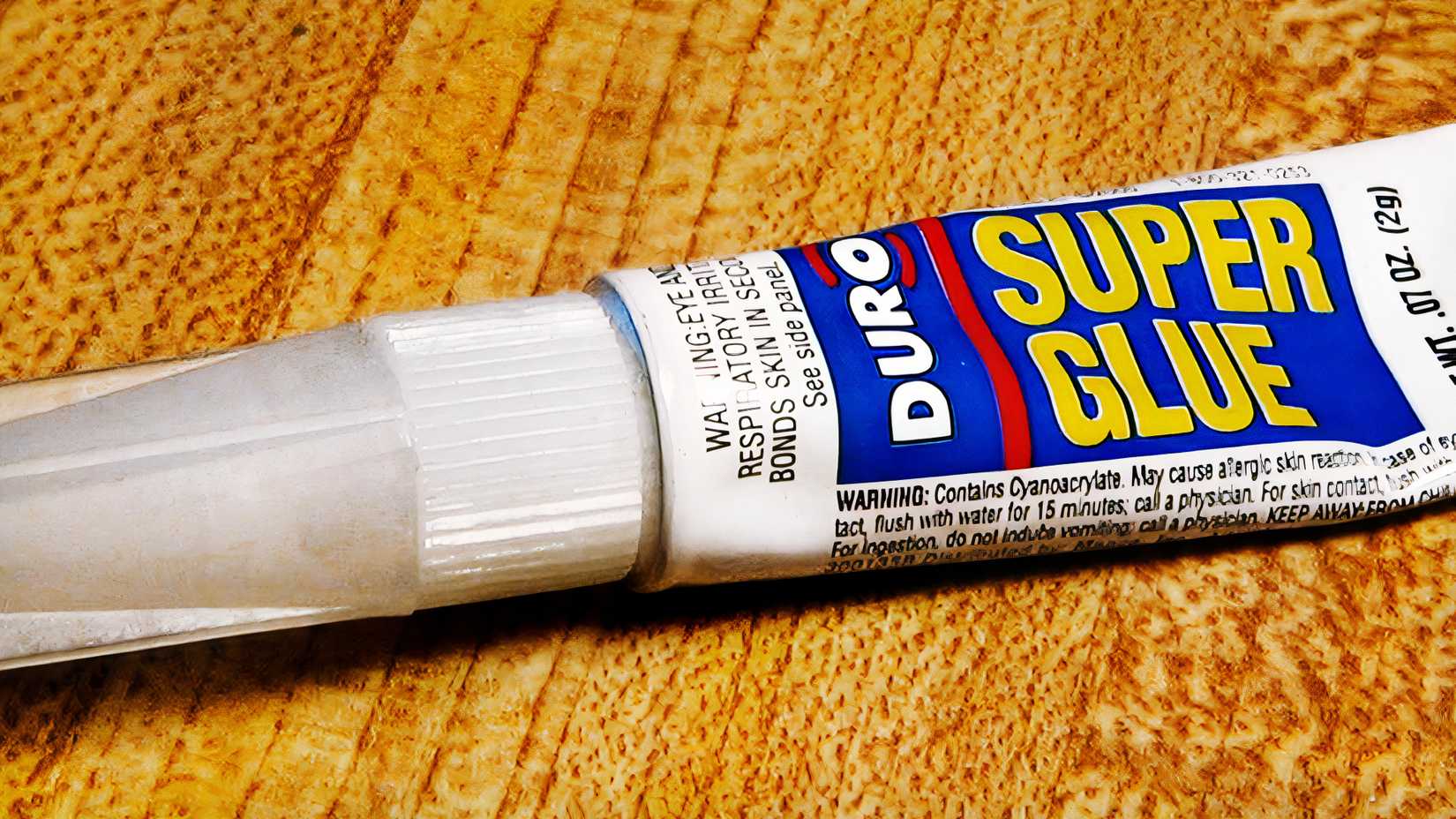 A tube of Duro Super Glue rests on a wooden surface.