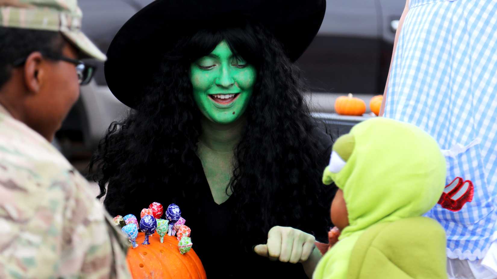 A costumed woman dressed as a witch hands candy to a child during a military family Halloween event at Fort Carson.