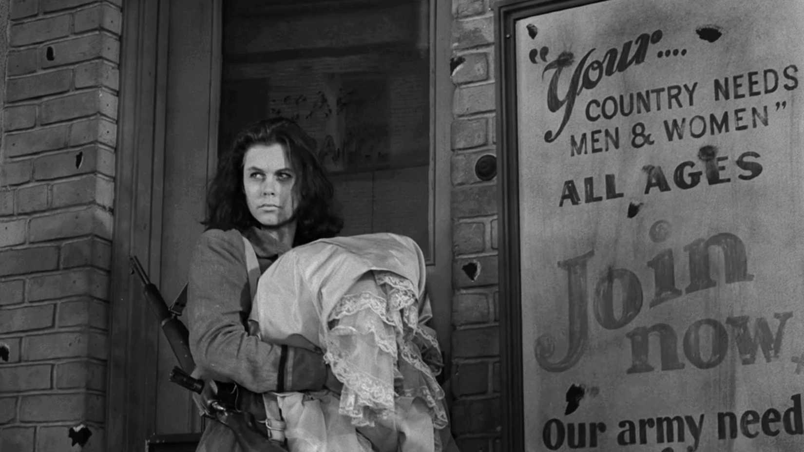 An armed woman carrying clothing stands outside a damaged building in The Twilight Zone episode “Two.”