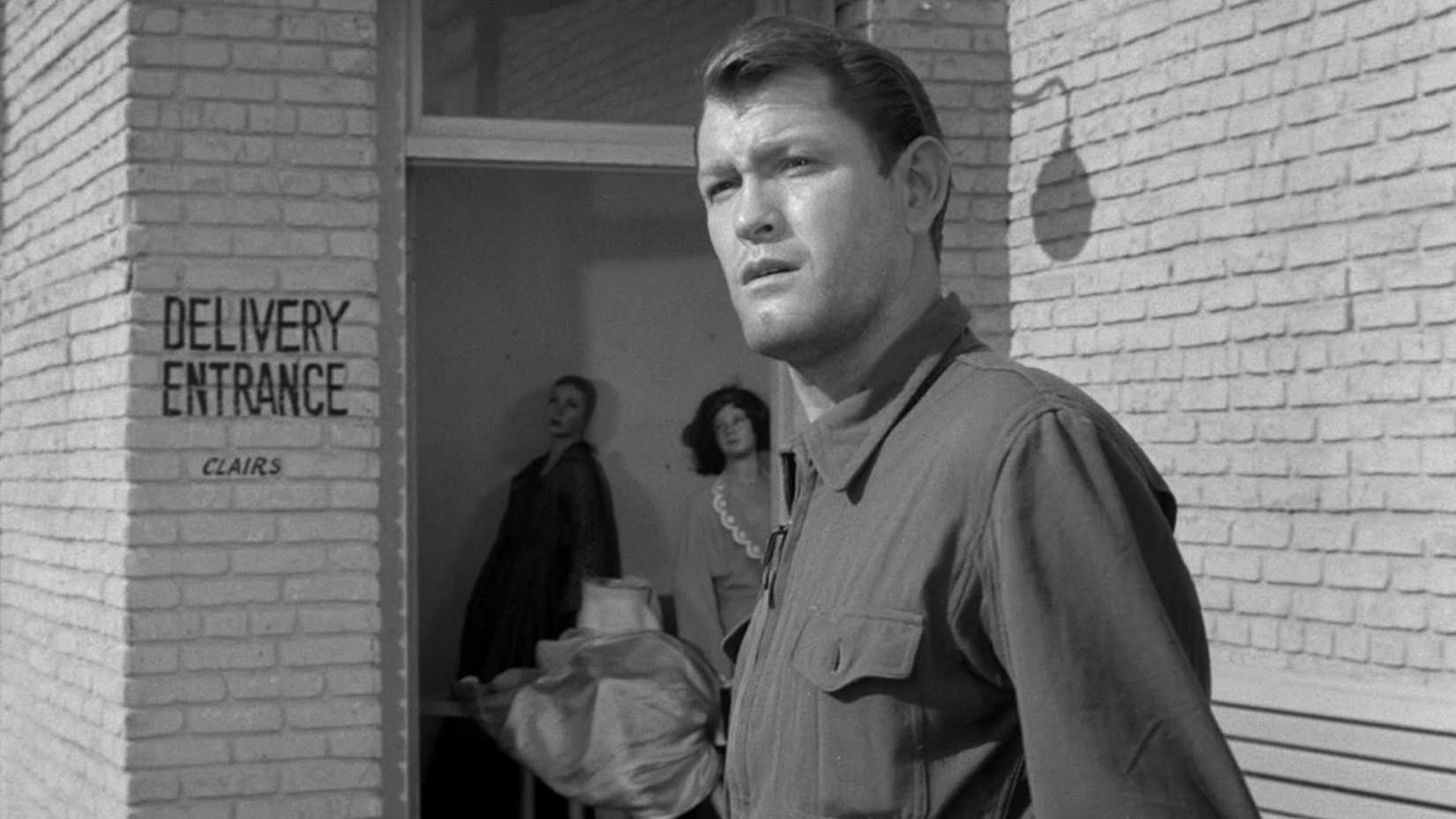 A man in work clothes stands outside a building in the deserted town of The Twilight Zone episode “Where Is Everybody?”